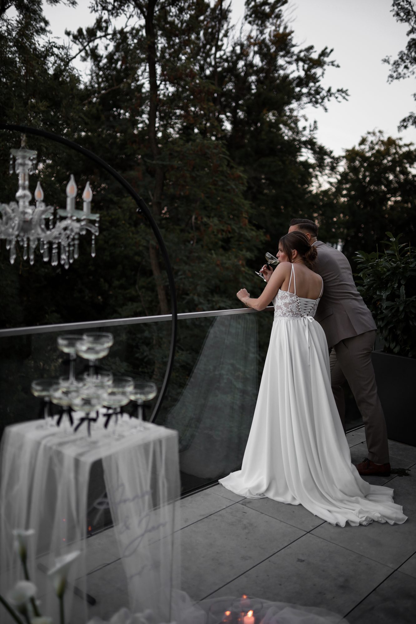 Brautpaar am Geländer einer Terrasse mit Champagner-Turm und Kronleuchter – Styled Shooting von Von Kraft Weddings
